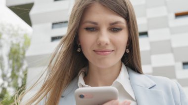 Sosyal medya uygulamasını akıllı telefon mesajlarında kullanan zarif genç bir bayana açık havada gülümseyen haberler geliyor. İnsan portreleri. Teknoloji. Kapalı kapılar ardında neşeli bir kız telefonda iyi haberler okuyor..