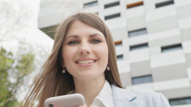 Sosyal medya uygulamasını akıllı telefon mesajlarında kullanan zarif genç bir bayana açık havada gülümseyen haberler geliyor. İnsan portreleri. Teknoloji. Kapalı kapılar ardında neşeli bir kız telefonda iyi haberler okuyor..