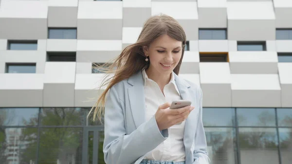 Adulte caucasien confiant jeune femme d'affaires en chemise blanche est apprécié sur téléphone à l'extérieur près de l'immeuble de bureaux moderne. Moyen long angle bas 4K Slow Motion prise de vue d'entreprise avec déplacement autour — Photo