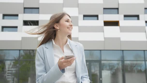 Dospělý kavkazský sebevědomý mladý obchodní žena v bílé košili se těší na telefonu mimo moderní kancelářské budovy. Střední dlouhý nízký úhel 4K pomalý pohyb korporátní střela s pohybem kolem — Stock video