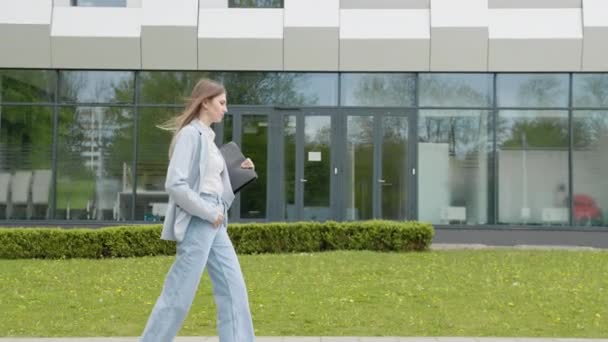 A girl in a business suit with a laptop in her hands walks down the street against the backdrop of a monumental building. Business. Social Network. Apps. Attractive business girl. Career people. — Stock Video