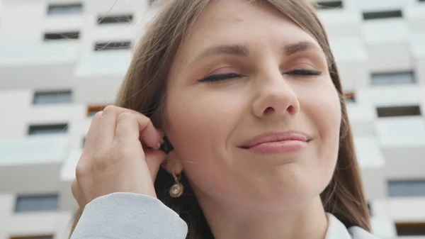 Joven mujer de negocios disfrutando de la música favorita de la lista de reproducción en el teléfono inteligente a través de auriculares modernos con buen sonido y estéreo disfrutando caminando por la calle. Chica joven saca los auriculares de la caja — Foto de Stock