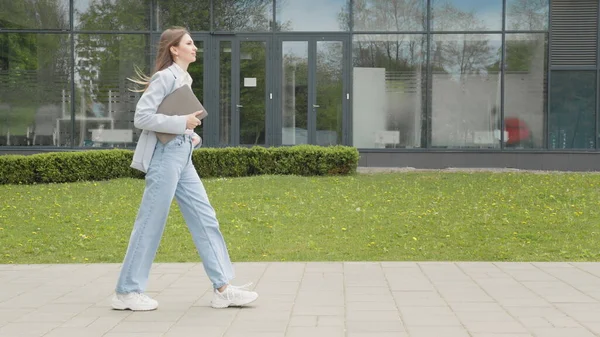 Una chica en un traje de negocios con un portátil en sus manos camina por la calle contra el telón de fondo de un edificio monumental. Negocios. Red Social. Aplicaciones. Una atractiva chica de negocios. Gente de carrera. — Foto de Stock