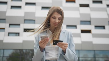 Elinde kredi kartı ve akıllı telefon tutan gülümseyen genç bayan müşteri. İnternetten alışveriş yapan mutlu bayan alışverişçi kolay taşınabilir ödemeler yapıyor. E-bankacılık uygulama servisi. İnternetten alışveriş.