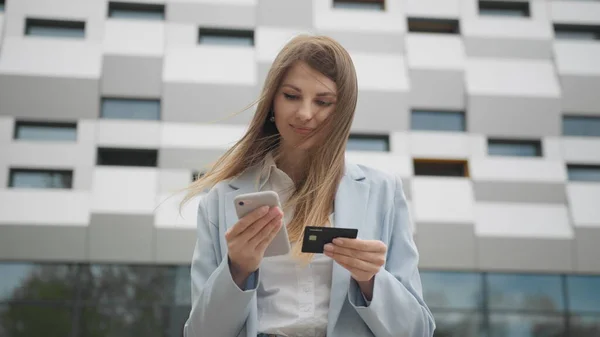 Hymyilevä nuori nainen asiakkaan tilalla luottokortti ja älypuhelin. Happy naaras shopper käyttäen instant helppo mobiilimaksut tehdä ostoksia verkkokaupasta. Sähköisen pankkipalvelun sovelluspalvelu. Verkkokauppa. tekijänoikeusvapaita kuvapankkikuvia
