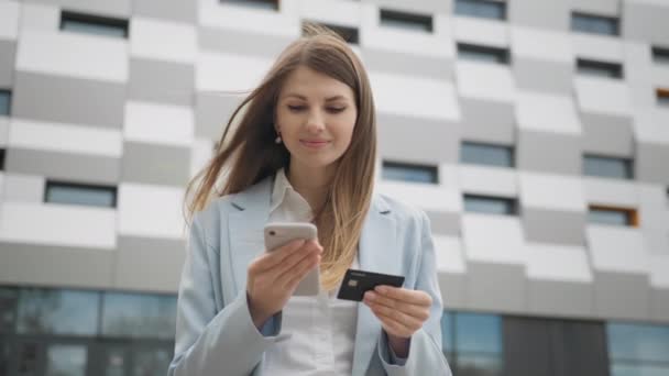 Sorrindo jovem cliente segurando cartão de crédito e smartphone. Comprador feliz do sexo feminino usando pagamentos móveis fáceis instantâneas fazendo compra na loja online. Serviço de E-banking app. Compras online. — Vídeo de Stock