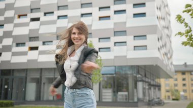 Şık giyimli kadın kot pantolonla dışarıda eğleniyor. Mutlu ve Sevimli görünüyorsun. Kasabada zıplayıp koşmak. Muhteşem görünüyorsun. Bir binanın arka planında bayan öğrencinin portresi