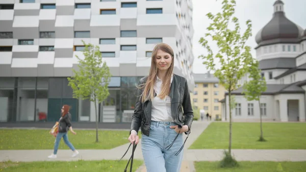 Menina estudante com mochila andando para o prédio da universidade. Feliz e sorridente, olhando para a câmera e caminhando para a frente. Retrato de Estudante Feminina em T-shirt Branca Olhando Confiantemente para a Câmera — Fotografia de Stock