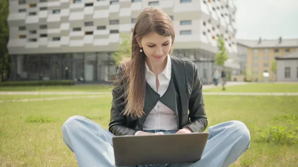 Happy woman working on laptop computer on green lawn in summer park. Young woman freelancer happy to receive new order. Female student using notebook outdoor. Teenage girl reading good news on laptop