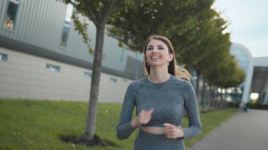 Summer Park City 'de koşucu eğitimi alan genç bir kadın. Şehir merkezindeki boş caddede koşan ve yalnız koşan genç ve zinde bir kadının portresi. Koruyucu giysisiyle. Yavaş çekim.