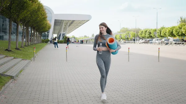 Flickan springer nerför trappan i slow motion. Löpare kvinna som springer på trappor vid utomhus träning. Ung sportig vacker flicka med en matta i händerna och vatten, kör uppför trappan i centrum — Stockfoto