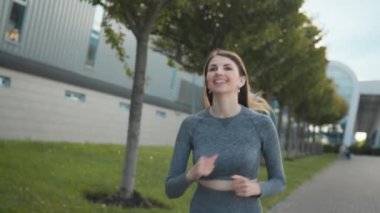 Summer Park City 'de koşucu eğitimi alan genç bir kadın. Şehir merkezindeki boş caddede koşan ve yalnız koşan genç ve zinde bir kadının portresi. Koruyucu giysisiyle. Yavaş çekim.