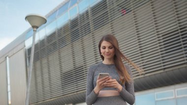 Çekici ve mutlu kızın POV 'u. Smartphone Tutan Güzel Bir Spor Kızının Yakın Çekimi. Kafkasyalı genç kadının modern binanın arka planında görüntülü konuşma yaparken yakın plan. Açık havada. bir