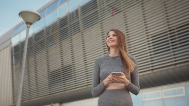 Açık havada koşarken akıllı telefona bakan portre kadını. Spor salonundaki genç ve güzel bir kızın elinde akıllı bir telefon tutarak spor uygulaması kullanmasının yakın çekimi. Modern Şehir Sokakta Çekim