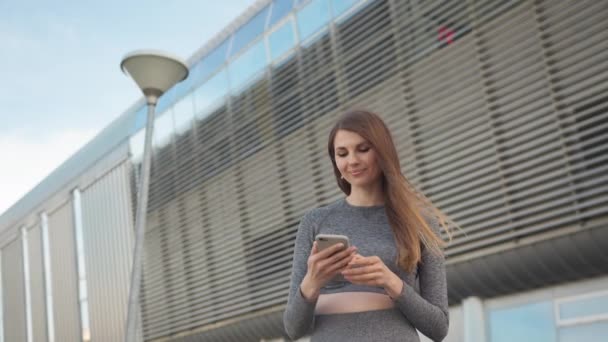 POV da menina encantadora e feliz. Close-up de uma bela garota de esportes segurando um smartphone. Close up da jovem mulher caucasiana tendo um bate-papo por vídeo sobre o fundo do edifício moderno. Ao ar livre. um — Vídeo de Stock