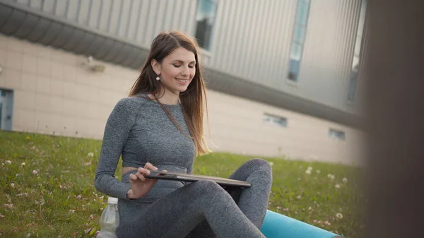 Donna attraente occupata che lavora al computer portatile come seduta su erba in parco di città. Studente che studia all'aperto. Libero professionista che lavora nel parco. Atletica ragazza fitness durante l'allenamento di lavoro a distanza — Foto Stock