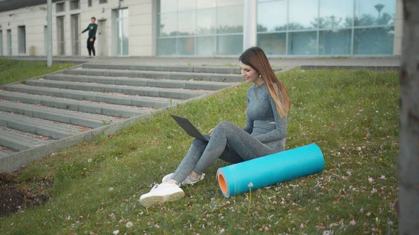Šťastná žena, sedí venku na laptopu. Usmívající se fit dívka psaní na notebooku na pozadí města. Osoba pracující venku na laptopu. Atraktivní dívka, firemní startup office zaměstnanec pracující venku — Stock fotografie