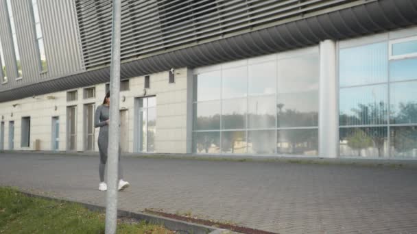 Deportiva hermosa joven camina lentamente en la ciudad sosteniendo un teléfono en sus manos y sonríe. Alegre caucásico entrenador de fitness mujer usando el teléfono móvil de las redes sociales sonriendo mientras. — Vídeos de Stock