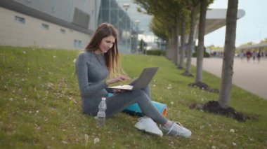 Açık havada dizüstü bilgisayar kullanan bir kadın portresi. İş kadını laptopta çalışıyor, yaz parkında yoga dersini bekliyor. Sağlıklı yaşam tarzı kavramı. Çalışma ve Eğitim