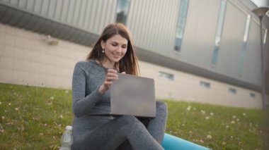 Şehir parkında çimlerin üzerinde oturan laptopta çalışan çekici bir kadın. Öğrenci dışarıda okuyor. Parkta çalışan serbest çalışan biri. Egzersiz sırasında spor yapan kız uzaktan çalışıyor.