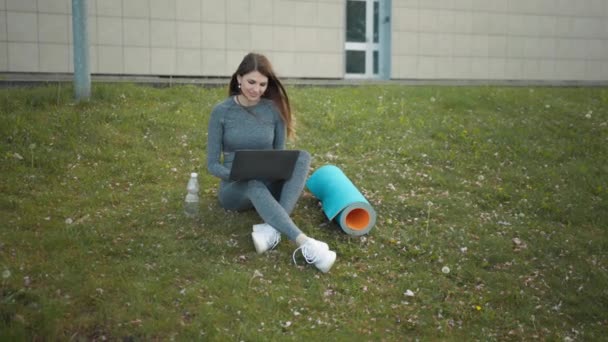 Glad kvinna, sittandes laptop utomhus. Leende passform flicka skriva på bärbar dator på city bakgrund. Person som jobbar på laptop utanför. Attraktiv tjej, företag start kontor anställd arbetar utomhus — Stockvideo