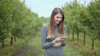 Dışarıda cep telefonuyla yazan mutlu kadın. Arka planda akıllı telefonu olan neşeli bir kız. Dışarıda cep telefonunu tutan gülümseyen kadın. Atletik fitness kızı elinde telefon tutuyor..