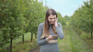 Dışarıda cep telefonuyla yazan mutlu kadın. Arka planda akıllı telefonu olan neşeli bir kız. Dışarıda cep telefonunu tutan gülümseyen kadın. Atletik fitness kızı elinde telefon tutuyor..