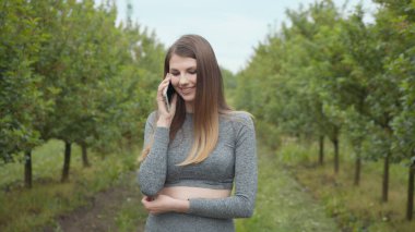 Dışarıda cep telefonuyla yazan mutlu hippi kadın. Ağaçların arka planında akıllı telefonu olan neşeli bir kız. Dışarıda cep telefonunu tutan gülümseyen kadın. Kız telefonla iletişim kuruyor.