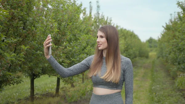 Una donna sportiva moderna scatta foto sullo smartphone della natura, registrando un video blog. Video sportivo vlog. Atleta del Video Blog. Ragazza blogger indica la natura della fotocamera — Foto Stock