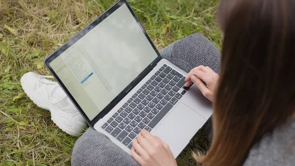 Top view Girl jobber med laptop på gaten og sitter på gresset. Jentestudent eller Freelancer forbereder arbeid, sorterer filer på datamaskinen, jobber hjemmefra og på kontoret. Håndtastatur – stockfoto