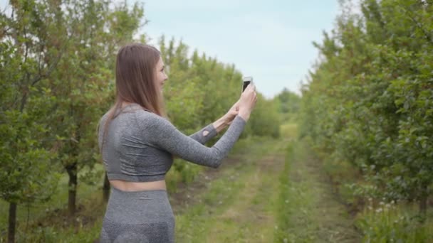 Jonge aantrekkelijke sport meisje schieten op een telefoonboom gefotografeerd tegen de achtergrond van de natuur. Girl blogger wijst op de camera natuur, het concept van verhalen over de bescherming van het milieu van bomen — Stockvideo