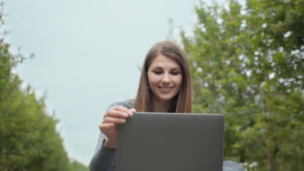 Γυναίκα άνοιγμα υπολογιστή laptop και αρχίζουν να πληκτρολογούν στο πληκτρολόγιο, δέντρα στη φύση. Οι γυναίκες που ασχολούνται με επιχειρήσεις ή freelance στη φύση ή φρέσκο αέρα στο καταπληκτικό φως του ήλιου. Κορίτσι που κάθεται στο πάρκο ή στο δάσος — Αρχείο Βίντεο