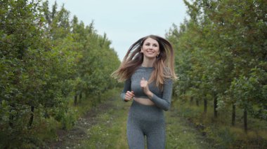 Yaz parkında genç bayan koşucu eğitimi. Spor salonundaki kadın dışarıda koşuyor. Sağlıklı koşu ve açık hava egzersizlerini, oyuncak bebek vuruşlarını hesaba katın. Spor Giyim 'deki Genç Formalı Kadın. Yavaş Hareket