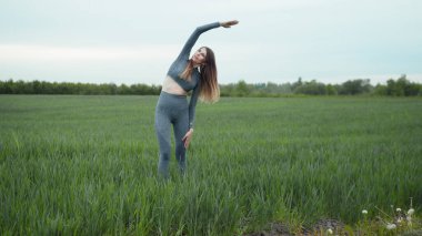 Kadın esneme ve ısınma koşusundan önce. Spor Giyim ve Isınma Antrenmanı. Açık havada spor yapan bir kadın. Koşu yaptıktan sonra kollarını esneten ve esneten bir kız..