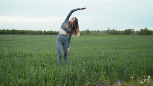 Kadın esneme ve ısınma koşusundan önce. Spor Giyim ve Isınma Antrenmanı. Açık havada spor yapan bir kadın. Koşu yaptıktan sonra kollarını esneten ve esneten bir kız..
