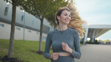 Summer Park City 'de koşucu eğitimi alan genç bir kadın. Şehir merkezindeki boş caddede koşan ve yalnız koşan genç ve zinde bir kadının portresi. Koruyucu giysisiyle. Yavaş çekim.