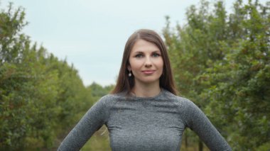 Mutlu, güzel, sağlıklı bir kızın portresi spor giyimli, spor kıyafetli, açık havada spor salonuna giden ve gülümseyen, kameraya bakan genç bir kadın. Yeni normal açık hava sporu.