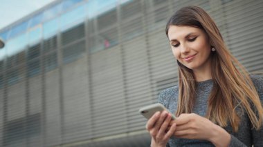 Spor salonundaki genç ve güzel bir kızın elinde akıllı bir telefon tutarak spor uygulaması kullanmasının yakın çekimi. Modern Şehir Sokakta Çekim. Açık havada koşarken akıllı telefona bakan portre kadını.