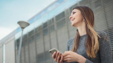 Spor salonundaki genç ve güzel bir kızın elinde akıllı bir telefon tutarak spor uygulaması kullanmasının yakın çekimi. Modern Şehir Sokakta Çekim. Açık havada koşarken akıllı telefona bakan portre kadını.