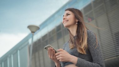 Fitness, spor ve teknoloji konsepti - mutlu bir gülümseme ile dışarı koşan kadın. Elinde akıllı bir telefon tutan genç ve güzel bir spor jimnastik kızının yakın çekimi. Eğitim sırasında telefon görüşmesi