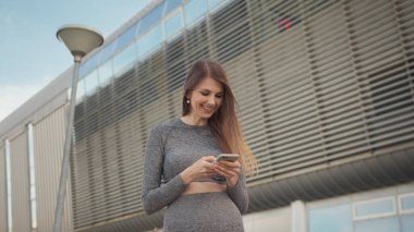 Açık havada koşarken akıllı telefona bakan portre kadını. Spor salonundaki genç ve güzel bir kızın elinde akıllı bir telefon tutarak spor uygulaması kullanmasının yakın çekimi. Modern Şehir Sokakta Çekim