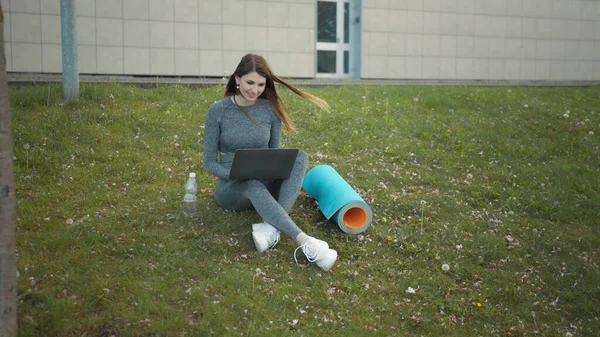 Happy woman, sitting laptop outdoor. Smiling fit girl typing on laptop computer at city background. Person working on laptop outside. Attractive girl, corporate startup office employee working outdoor