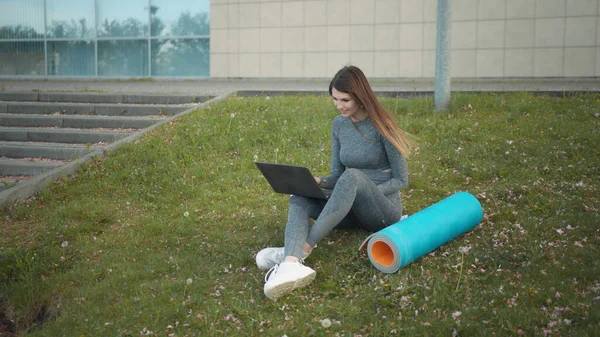 Happy woman, sitting laptop outdoor. Smiling fit girl typing on laptop computer at city background. Person working on laptop outside. Attractive girl, corporate startup office employee working outdoor