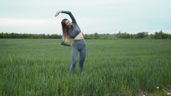 Kadın esneme ve ısınma koşusundan önce. Spor Giyim ve Isınma Antrenmanı. Açık havada spor yapan bir kadın. Koşu yaptıktan sonra kollarını esneten ve esneten bir kız..