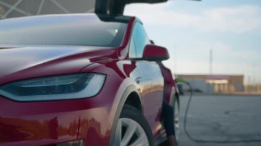Modern istasyonda kırmızı lüks elektrikli araba şarj ediliyor. Yeşil kablo otomatik sokete takıldı. Ulaşım, ekoloji ve yenilik kavramı. Elektrik kablosu dolgulu otomatik.