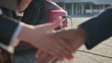 Adam elektrikli araba alırken bir kadınla tokalaşıyor. Afrikalı işadamı başarılı bir anlaşmadan sonra Müslüman kadınla tokalaşıyor. Arka planda kırmızı elektrikli araba şarj oluyor. Satma ve satın alma kavramı