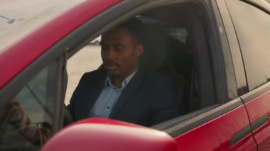 Afrikalı Amerikalı işadamı lüks elektrikli arabasının içinde. Yakışıklı adam başarılı bir alımdan memnun görünüyor. Çevre dostu araç kavramı. Satıcı yeni elektrikli arabadaki adama anahtarları veriyor.