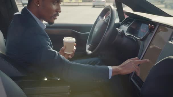 Vista lateral do homem africano focado sentado no assento dos motoristas com xícara de café e usando painel para navegação. Empresário em desgaste formal tendo parada para verificar a direção. Homem sentado no carro — Vídeo de Stock