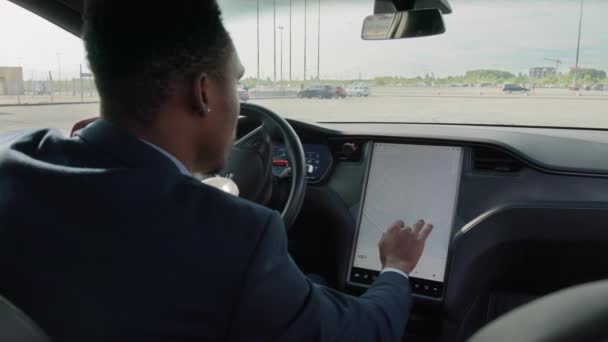 電動車の運転席に座って、指でダッシュボードに触れるスーツでアフリカの男を閉じます。ナビゲーションのための高級車の近代的なシステムを使用して若い男。方向の確認 — ストック動画