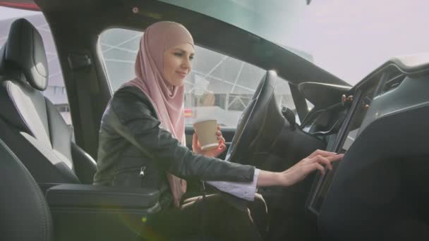 Vista lateral da mulher muçulmana no hijab tocando no painel eletrônico do carro de luxo enquanto tem uma conversa móvel. Conceito de tecnologia moderna, pessoas e transportes. Mulher tocando painel — Vídeo de Stock